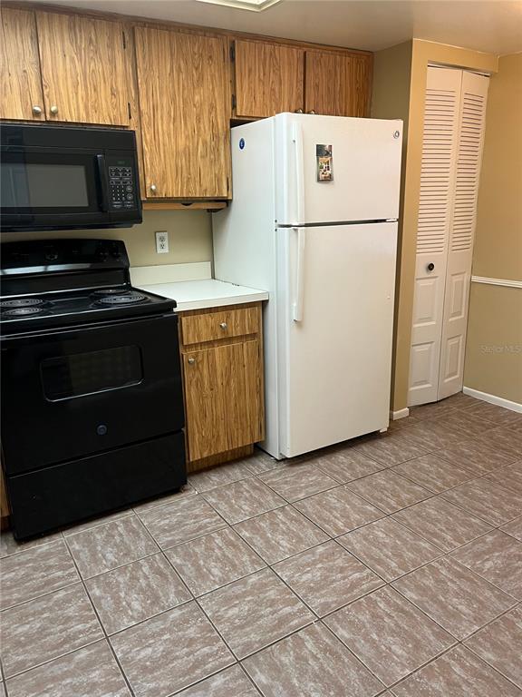 A kitchen features wood cabinets, black appliances, a white refrigerator, and brown tiled flooring — 39650 US HIGHWAY 19 N UNIT 576, TARPON SPRINGS, FL