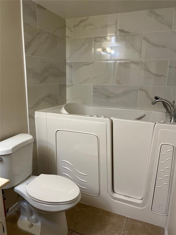 A bathroom features a white walk-in bathtub with marble-look tile walls next to a toilet — 39650 US HIGHWAY 19 N UNIT 576, TARPON SPRINGS, FL