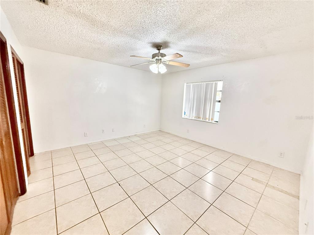 An empty room features white walls, a ceiling fan, and light-colored square floor tiles — 8336 JACKSON SPRINGS ROAD, TAMPA, FL
