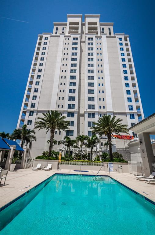 A tall, multi-story apartment building stands behind a rectangular outdoor swimming pool with lounge chairs — 331 CLEVELAND STREET UNIT 1101, CLEARWATER, FL