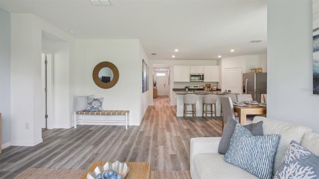 An open-concept living area features light wood-look flooring, a white kitchen, and coastal-style decor — 15018 CROSSHALL STREAM DRIVE, WIMAUMA, FL