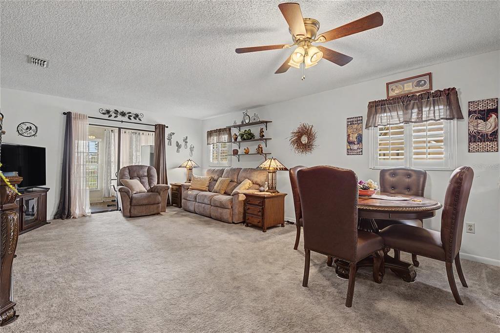 A carpeted living and dining room features a ceiling fan, sofa, recliner, and dining set — 38225 BOXWOOD DRIVE, ZEPHYRHILLS, FL