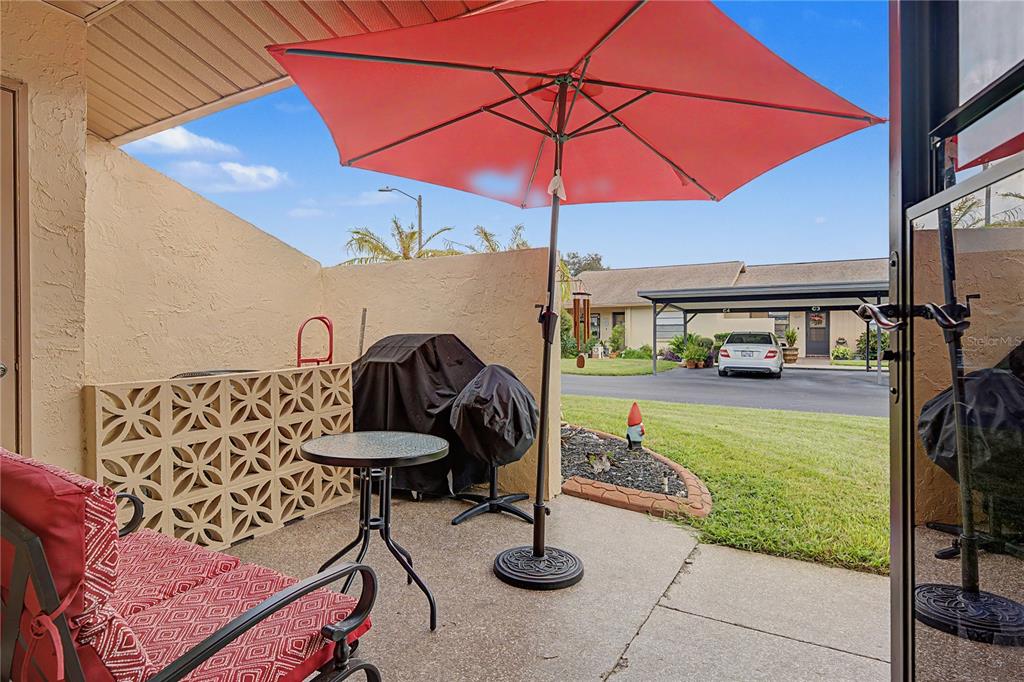 A patio with a red umbrella, a small table, and a grill overlooks a parking area — 38225 BOXWOOD DRIVE, ZEPHYRHILLS, FL