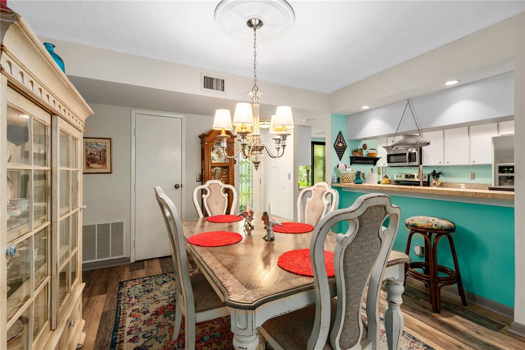 A dining room with a wooden table, chandelier, and an adjacent kitchen with turquoise walls — 1701 PELICAN COVE ROAD UNIT GL359, SARASOTA, FL