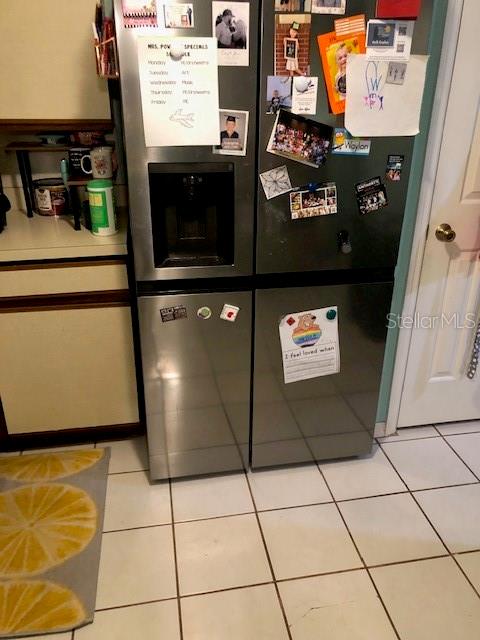 A stainless steel refrigerator covered in magnets and papers stands in a tiled kitchen — 2246 COACH HOUSE BOULEVARD UNIT 501, ORLANDO, FL