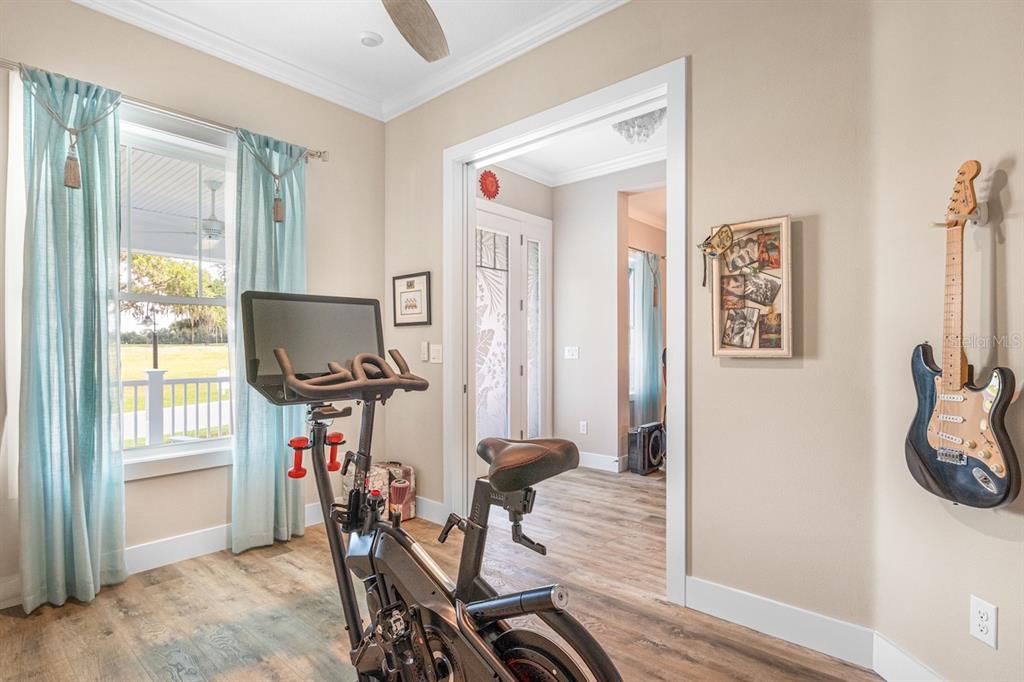 A home gym features a stationary bike, light wood flooring, and an electric guitar mounted — 1148 BAHIA HONDA KEY DRIVE, LADY LAKE, FL