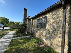 A stone-clad house exterior features a chimney and a dark-framed window under a clear sky — 1221 PERKINS ROAD, ORLANDO, FL