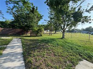 A grassy backyard features a concrete walkway, mature trees, and a chain-link fence — 1221 PERKINS ROAD, ORLANDO, FL