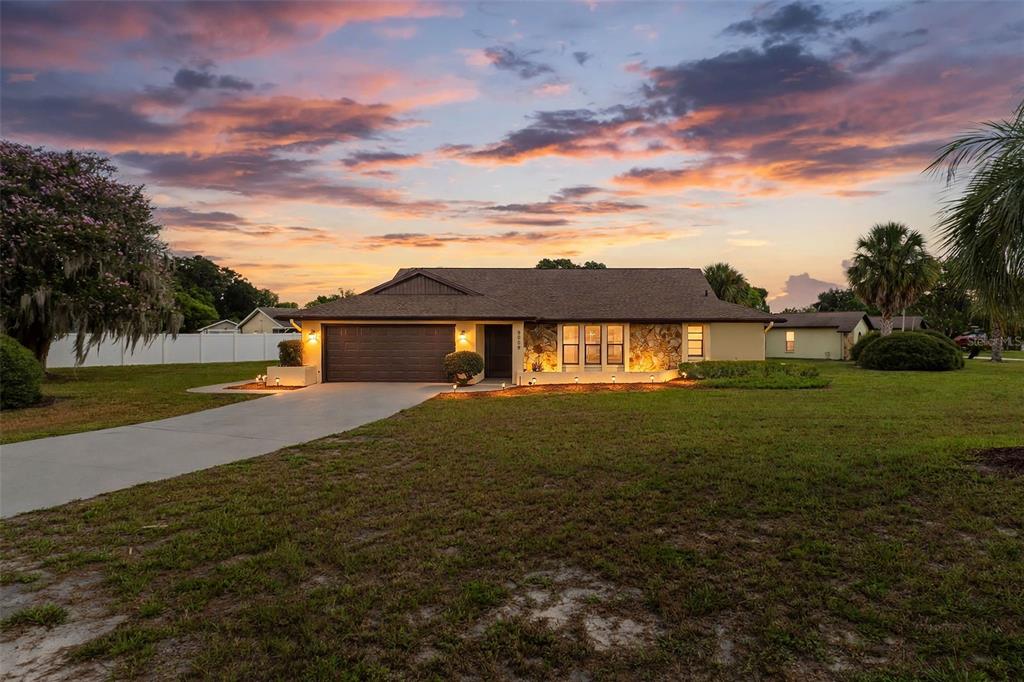 A single-story house with a brown garage, stone facade, and a sunset sky background — 9009 HEATHER BOULEVARD, WEEKI WACHEE, FL
