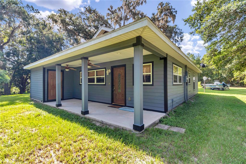 A gray house with a covered front porch, dark trim, and a wooden front door — 21497 NW 75TH AVENUE, MICANOPY, FL