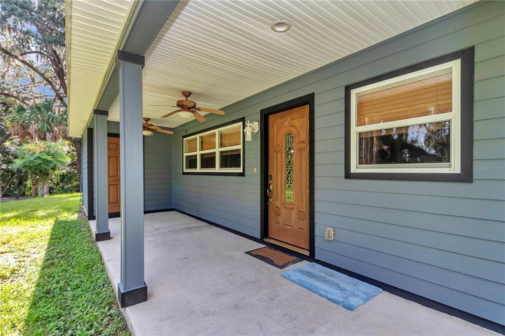 A covered porch with blue siding, a wooden front door, and two ceiling fans — 21497 NW 75TH AVENUE, MICANOPY, FL