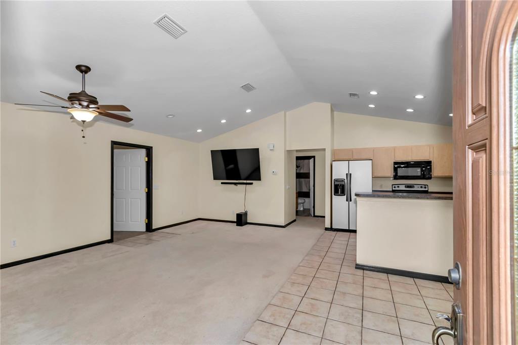 A living room with carpeted flooring, a ceiling fan, and an adjacent open kitchen area — 21497 NW 75TH AVENUE, MICANOPY, FL