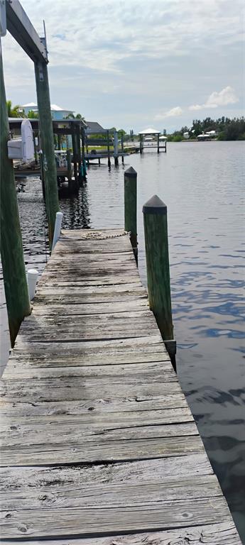 A weathered wooden dock extends over a calm canal toward other docks and distant homes — 819 BLUE HERON BOULEVARD, RUSKIN, FL