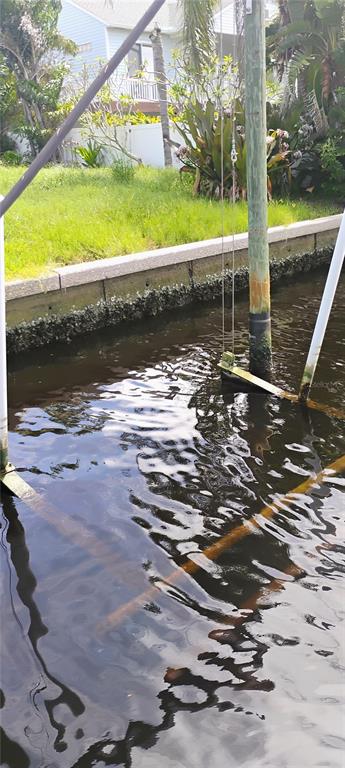 A wooden boat lift piling stands in a canal next to a concrete seawall and lawn — 819 BLUE HERON BOULEVARD, RUSKIN, FL