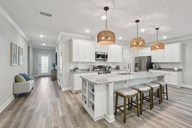 A modern kitchen features white cabinets, granite countertops, a large island, and three woven pendant lights — 5963 LYON ROAD, SPRING HILL, FL