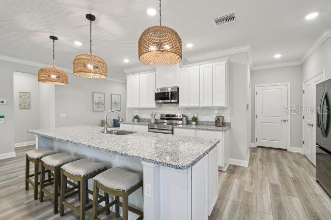 A kitchen features a granite-topped island with bar stools, white cabinetry, and three pendant lights — 5963 LYON ROAD, SPRING HILL, FL