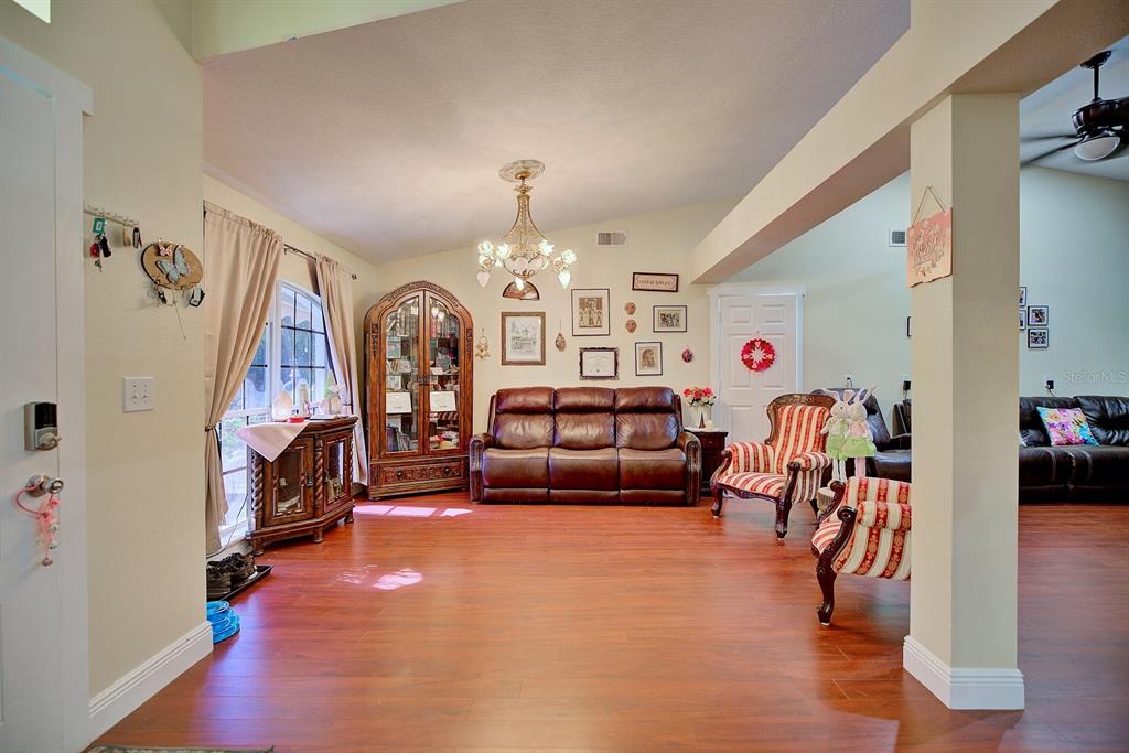 A living room with wood-look flooring, a leather sofa, a chandelier, and a display cabinet — 2478 THACKER TRAIL, KISSIMMEE, FL