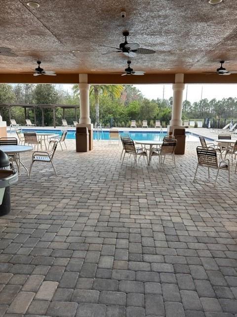 A covered outdoor patio with stone pavers, ceiling fans, and tables overlooking a swimming pool — 11048 SAVANNAH LANDING CIRCLE, ORLANDO, FL