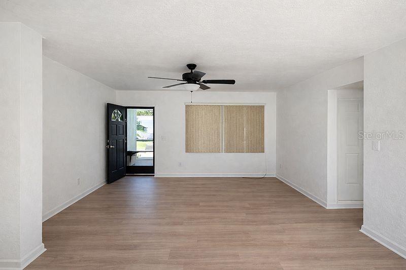 An empty living room features light wood-look flooring, white walls, a ceiling fan, and a door — 640 JASMINE ROAD, CASSELBERRY, FL
