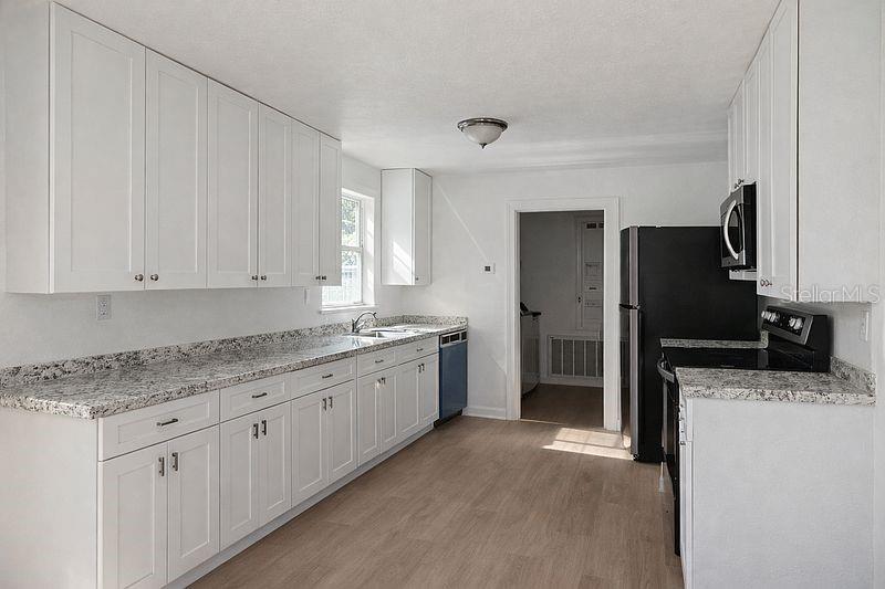 A kitchen features white cabinets, granite countertops, stainless steel appliances, and light wood-look flooring — 640 JASMINE ROAD, CASSELBERRY, FL