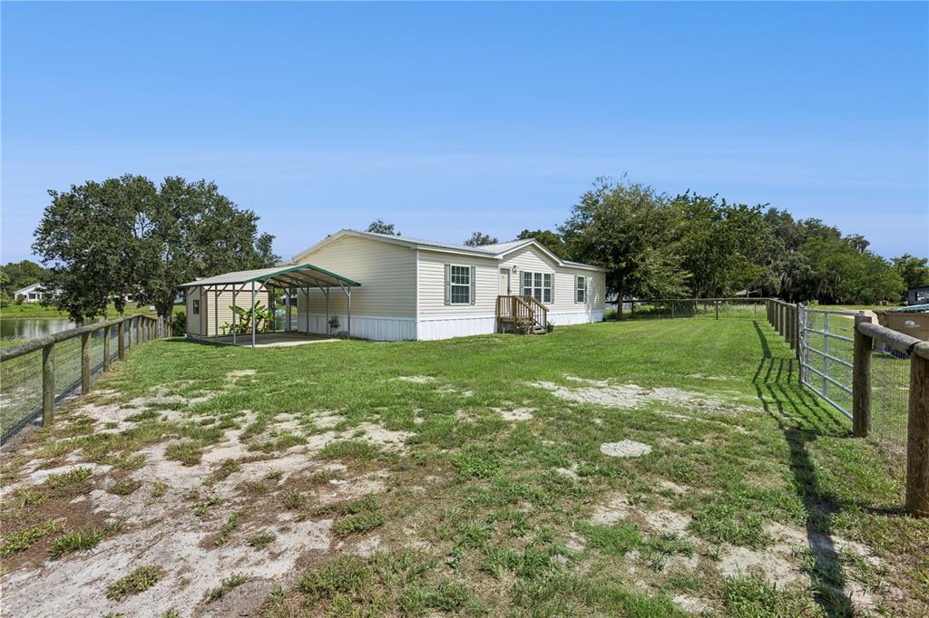 A single-story manufactured home features a metal carport and a fenced yard near water — 33525 LINDA DRIVE, LEESBURG, FL
