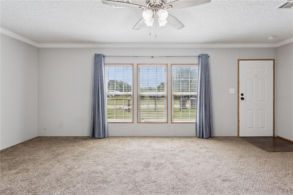 A carpeted living room features three windows with blue curtains and a ceiling fan — 33525 LINDA DRIVE, LEESBURG, FL