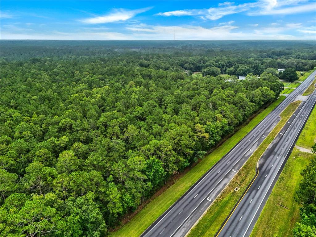 An aerial view shows a dense forest bordering a multi-lane highway under a blue sky — TBD NE NE 6TH AVENUE, LAWTEY, FL