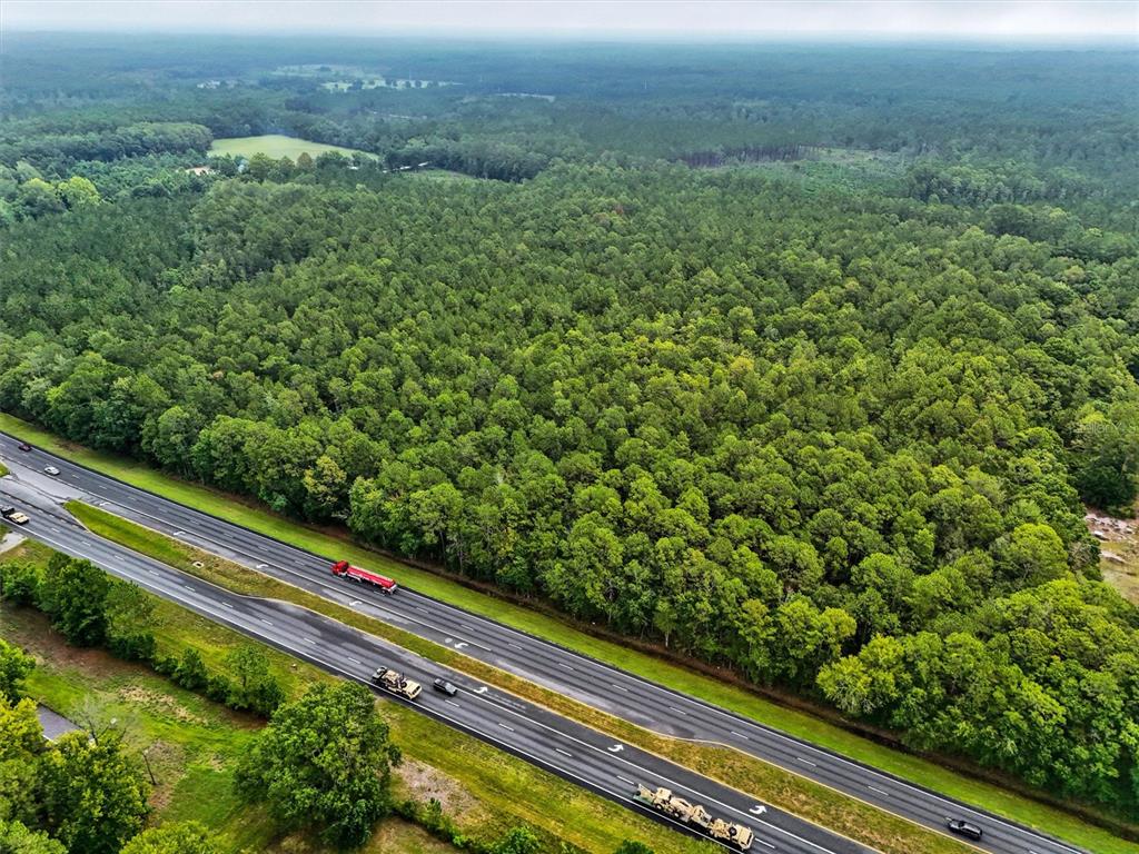 An aerial view shows a dense forest bordering a multi-lane highway with several vehicles — TBD NE NE 6TH AVENUE, LAWTEY, FL