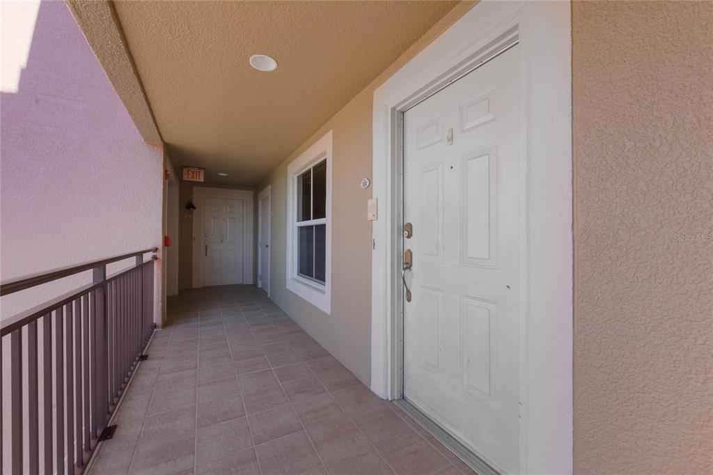 A tiled outdoor hallway leads to white apartment doors with a metal railing on the left — 424 LUNA BELLA LANE UNIT 332, NEW SMYRNA BEACH, FL