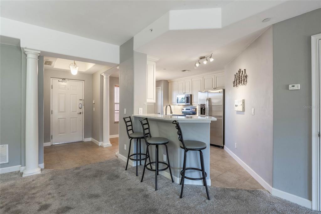 A kitchen with a breakfast bar and stools overlooks a carpeted living area and entryway — 424 LUNA BELLA LANE UNIT 332, NEW SMYRNA BEACH, FL