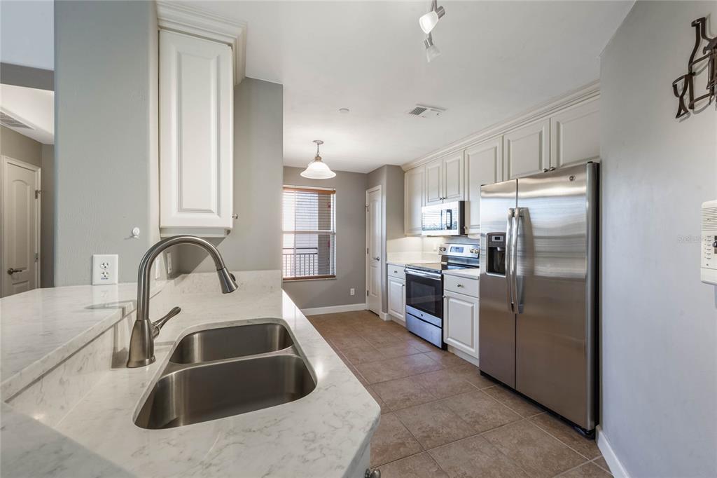 A kitchen with white cabinets, stainless steel appliances, and a marble-topped island with a sink — 424 LUNA BELLA LANE UNIT 332, NEW SMYRNA BEACH, FL