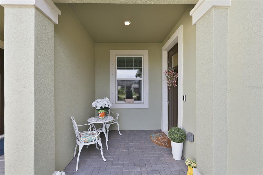 A covered front porch features a paver floor, two white chairs, and a small table — 12593 LILY QUARTZ LOOP, PARRISH, FL