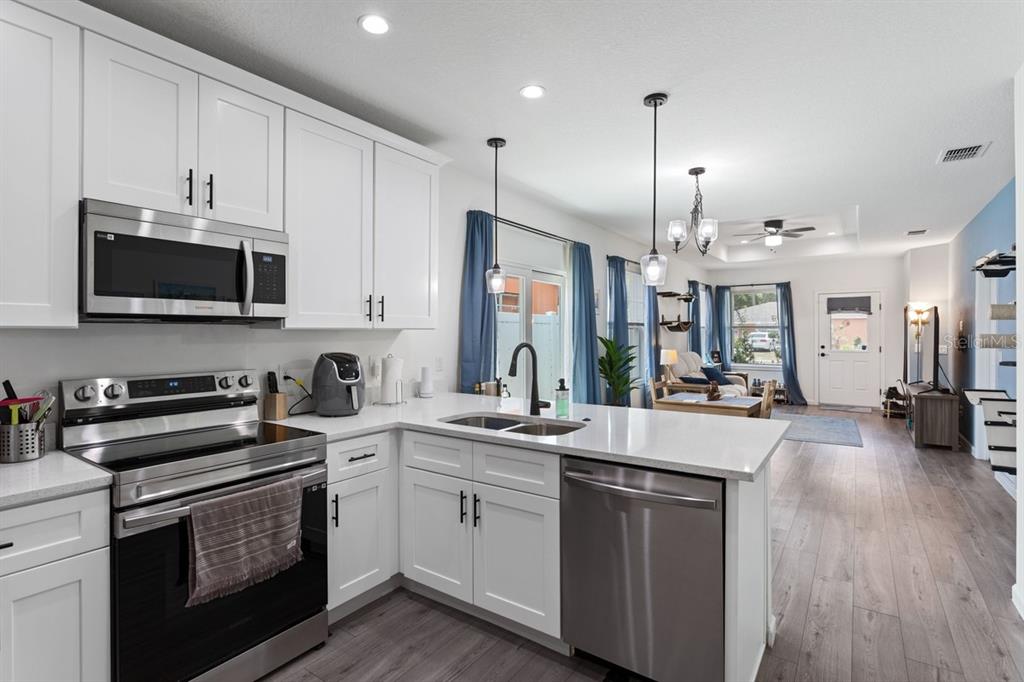 A modern kitchen with white cabinets, stainless steel appliances, and quartz countertops overlooks an open living area — 1967 VIRGINIA AVENUE, EUSTIS, FL