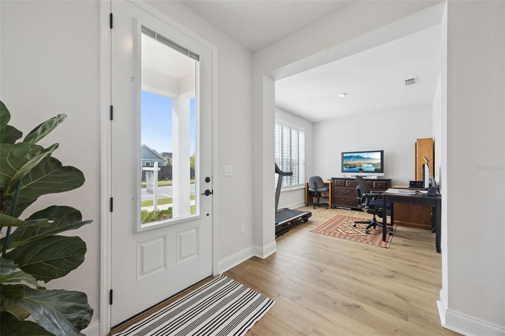 A bright entryway leads into a home office featuring wood-look flooring and a treadmill — 2954 JOURNEY PLACE, ST CLOUD, FL
