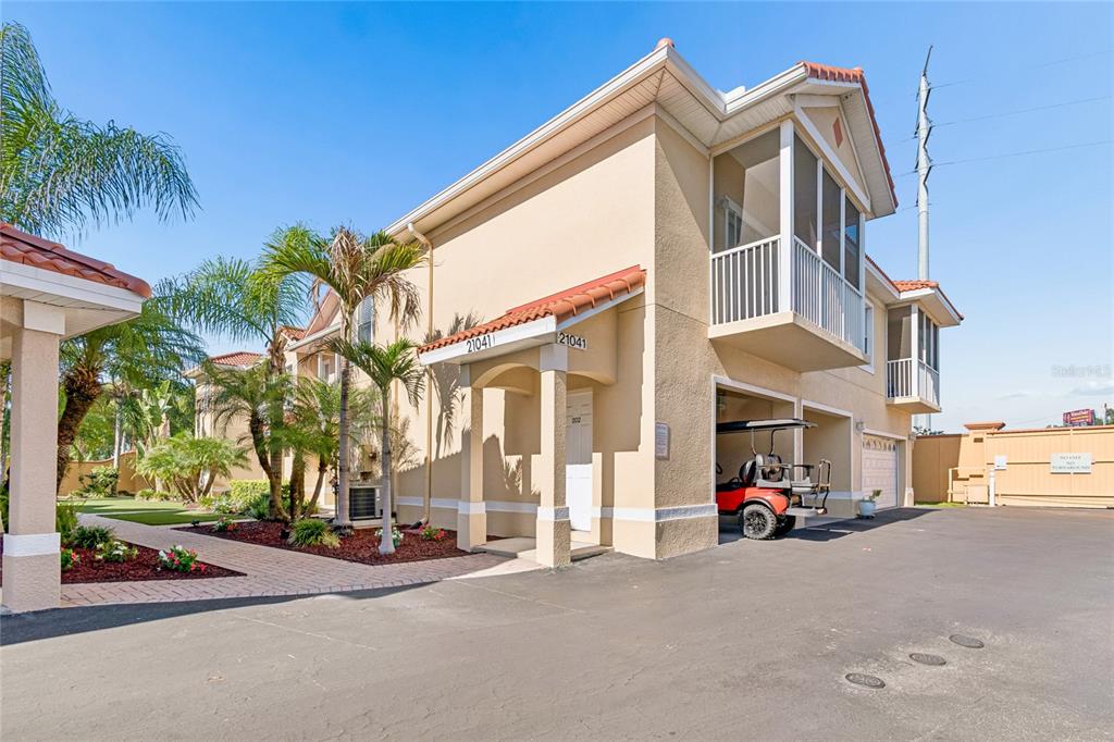 An exterior view of a two-story tan building with a golf cart parked underneath — 21041 SUNPOINT WAY UNIT 201, LUTZ, FL