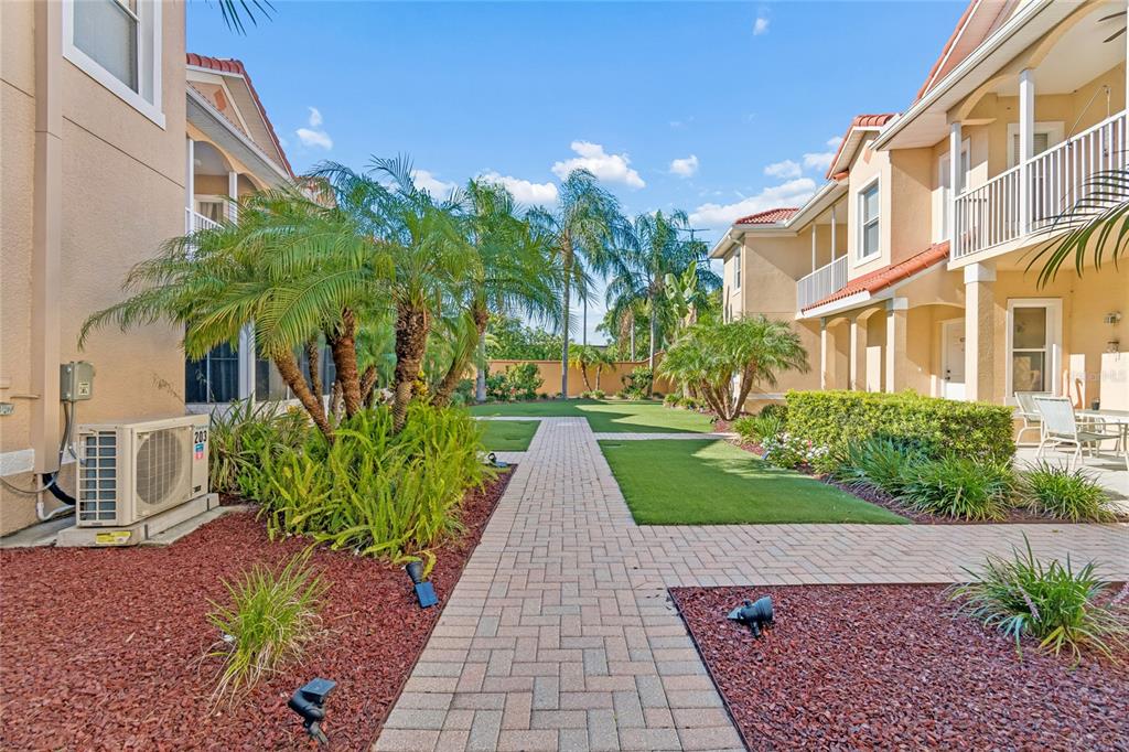 A paved walkway leads through a courtyard between two multi-story apartment buildings with palm trees — 21041 SUNPOINT WAY UNIT 201, LUTZ, FL