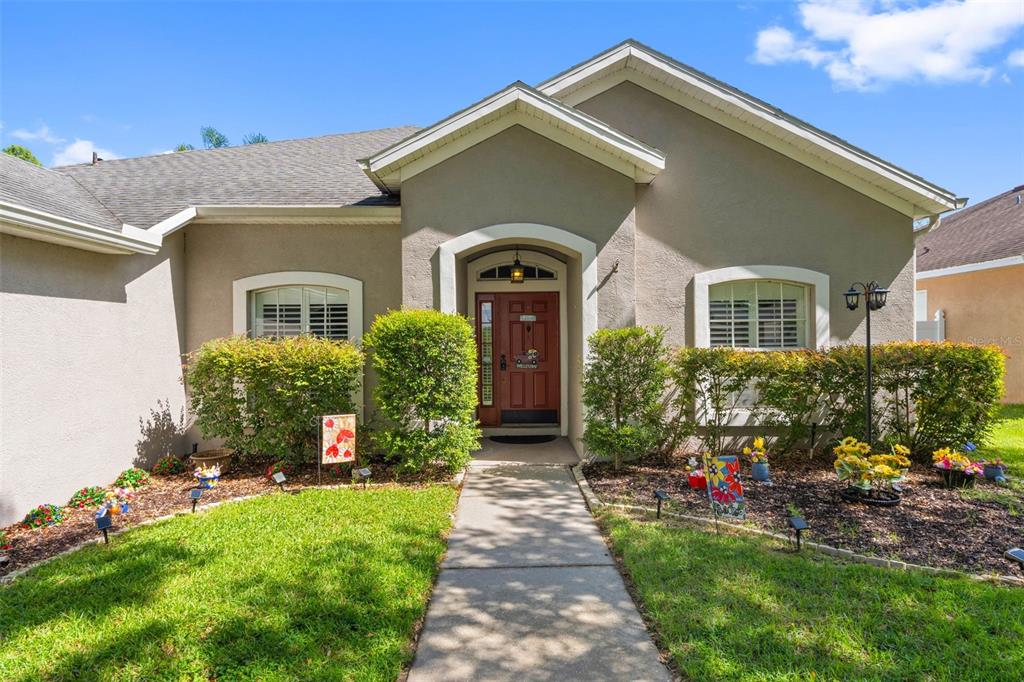 A single-story house with a beige stucco exterior, a red front door, and landscaped front yard — 11916 SUMMER SPRINGS DRIVE, RIVERVIEW, FL