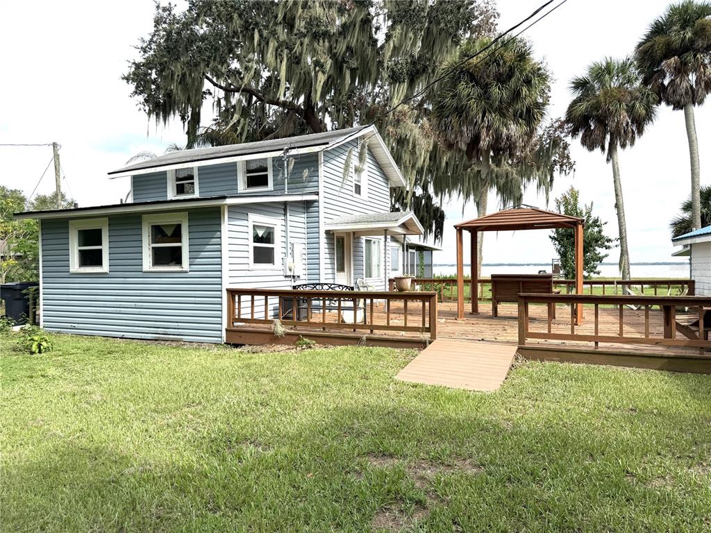 A two-story blue house with a large wooden deck overlooking a lake and palm trees — 1973 N LAKE REEDY BOULEVARD, FROSTPROOF, FL