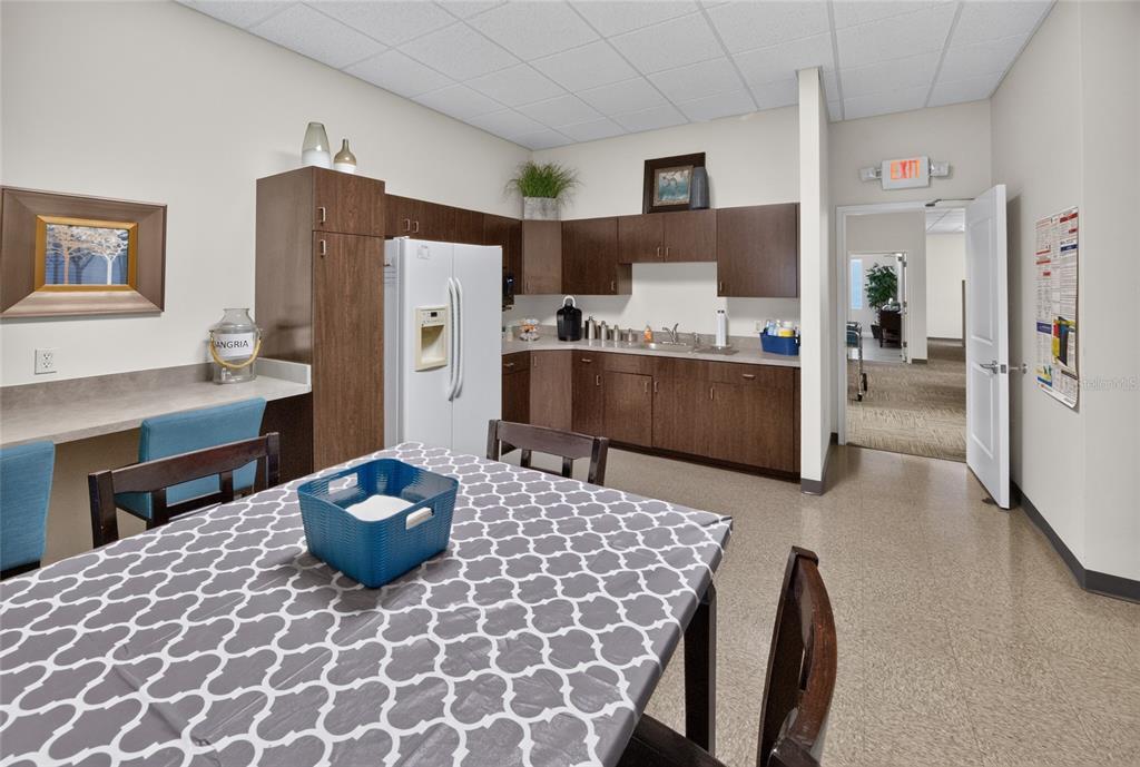 A breakroom features dark wood cabinetry, a white refrigerator, and a table with patterned seating — 840 & 842 HIGHWAY 466, LADY LAKE, FL