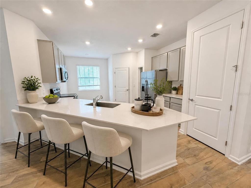 A kitchen features a white quartz island with bar seating, gray cabinetry, and light flooring — 836 TIMBERLAND DRIVE, EAGLE LAKE, FL