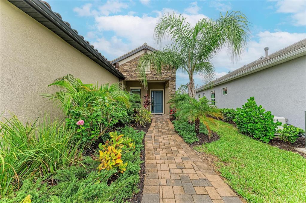A stone-accented house entrance features a paved walkway surrounded by lush landscaping and palm trees — 10913 TREVINO STREET, ENGLEWOOD, FL