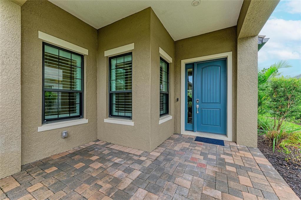 A blue front door with a side window sits on a paved porch with stucco walls — 10913 TREVINO STREET, ENGLEWOOD, FL