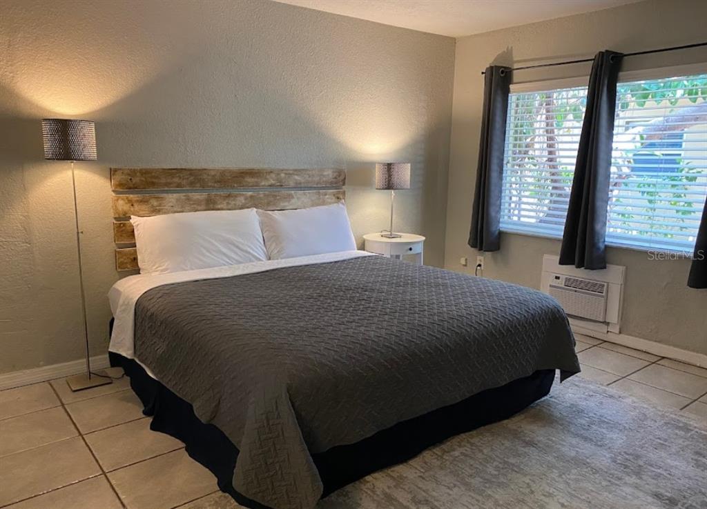A bedroom features a bed with a rustic wooden headboard, gray quilt, and tile flooring — 345 HAMDEN DRIVE, CLEARWATER BEACH, FL