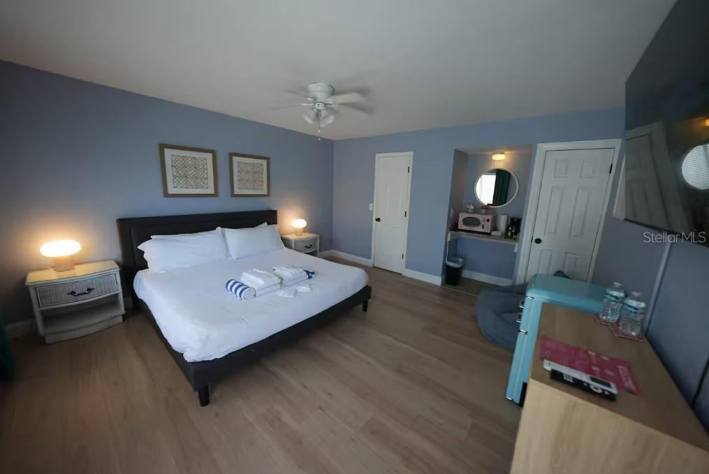 A bedroom with light blue walls, wood-look flooring, a king bed, and a small kitchenette area — 345 HAMDEN DRIVE, CLEARWATER BEACH, FL