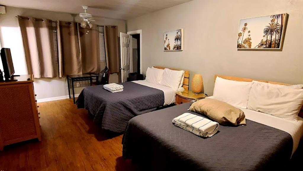 A bedroom features two beds with dark gray quilts, wood flooring, and two wall-mounted palm prints — 345 HAMDEN DRIVE, CLEARWATER BEACH, FL