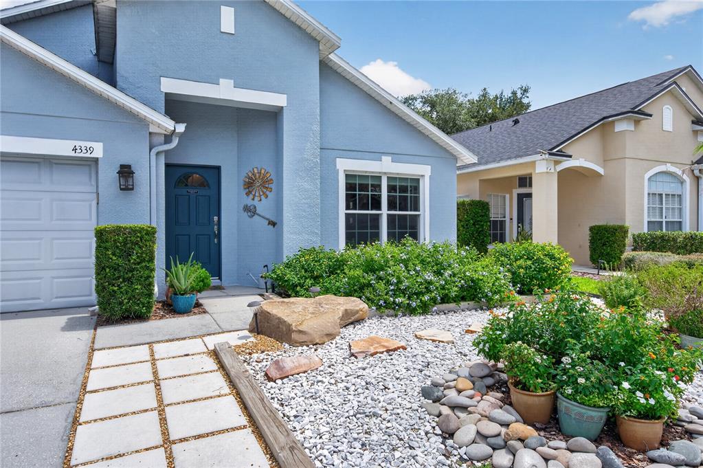 A light blue single-story house features a two-car garage, a blue front door, and landscaping — 4339 NORTHERN DANCER WAY, ORLANDO, FL