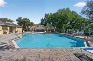 A rectangular swimming pool is surrounded by a brick patio and residential buildings — 6255 TIMBERLY LN, ZEPHYRHILLS, FL
