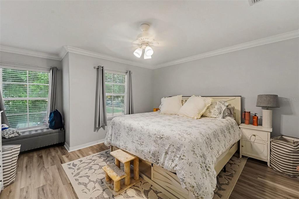 A bedroom features a bed with a floral comforter, a ceiling fan, and wood flooring — 6255 TIMBERLY LN, ZEPHYRHILLS, FL