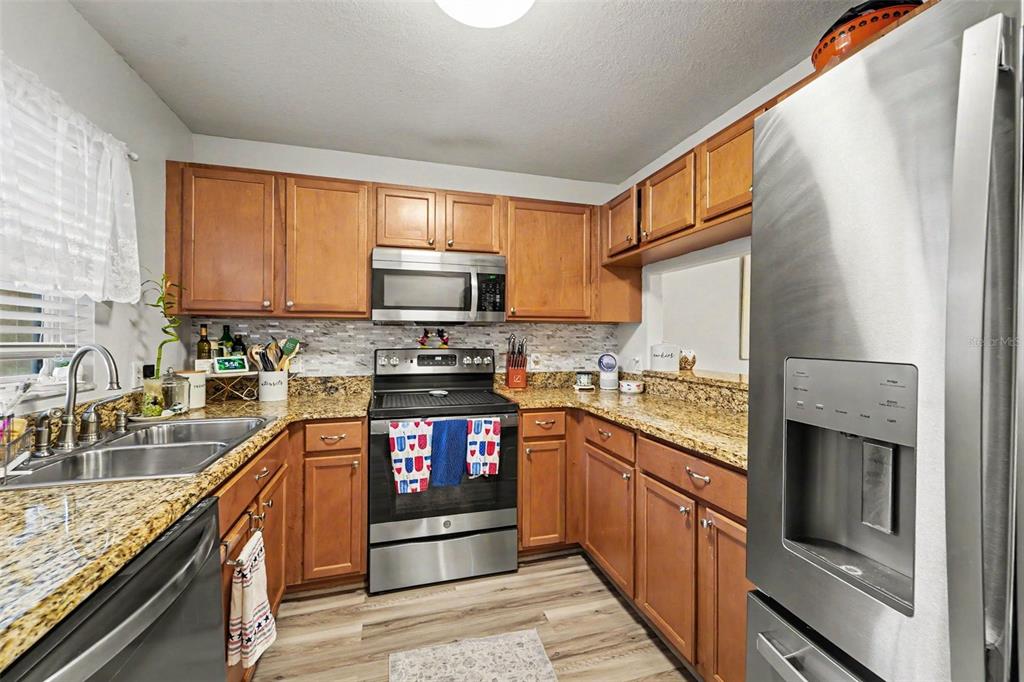 A kitchen features wood cabinets, granite countertops, stainless steel appliances, and light wood-look flooring — 6255 TIMBERLY LN, ZEPHYRHILLS, FL