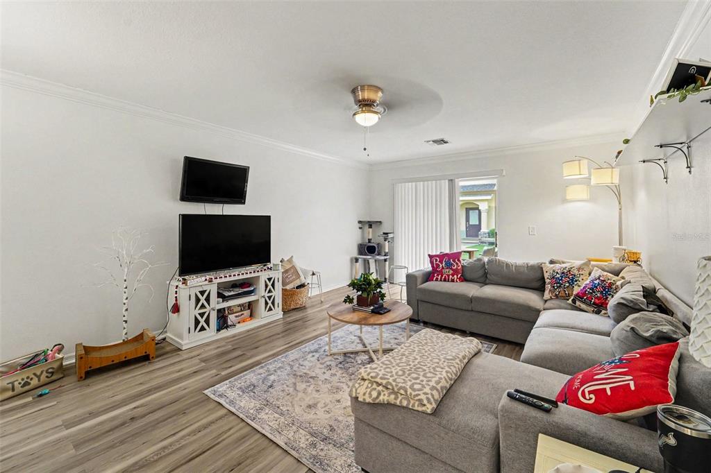A living room features a grey sectional sofa, a television console, and wood-look flooring — 6255 TIMBERLY LN, ZEPHYRHILLS, FL